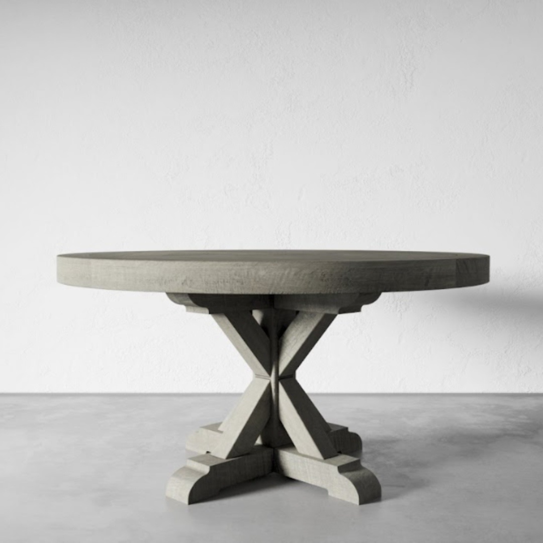 The Madera Round Table - Café Noire, featuring a robust and intricate pedestal base, stands on a gray concrete floor against a white textured wall.