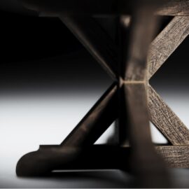 Close-up of the leg of a Madera Round Table with intricate detailing. The background is dark, highlighting the texture of the wood, reminiscent of a cozy Café Noire ambiance.