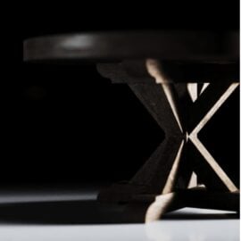 Low angle view of a Madera Round Table with an X-shaped base, partially illuminated against a dark background, reminiscent of the intimate ambiance at Café Noire.