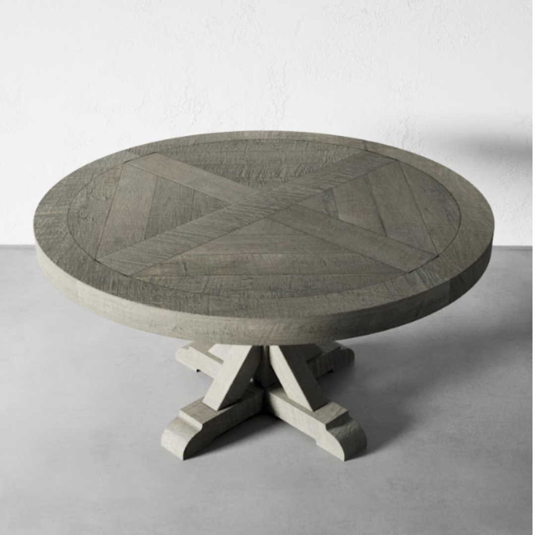Introducing the Madera Round Table - Café Noire, a round, grey wooden table featuring an elegant geometric X pattern on its surface and supported by a stylish pedestal base.