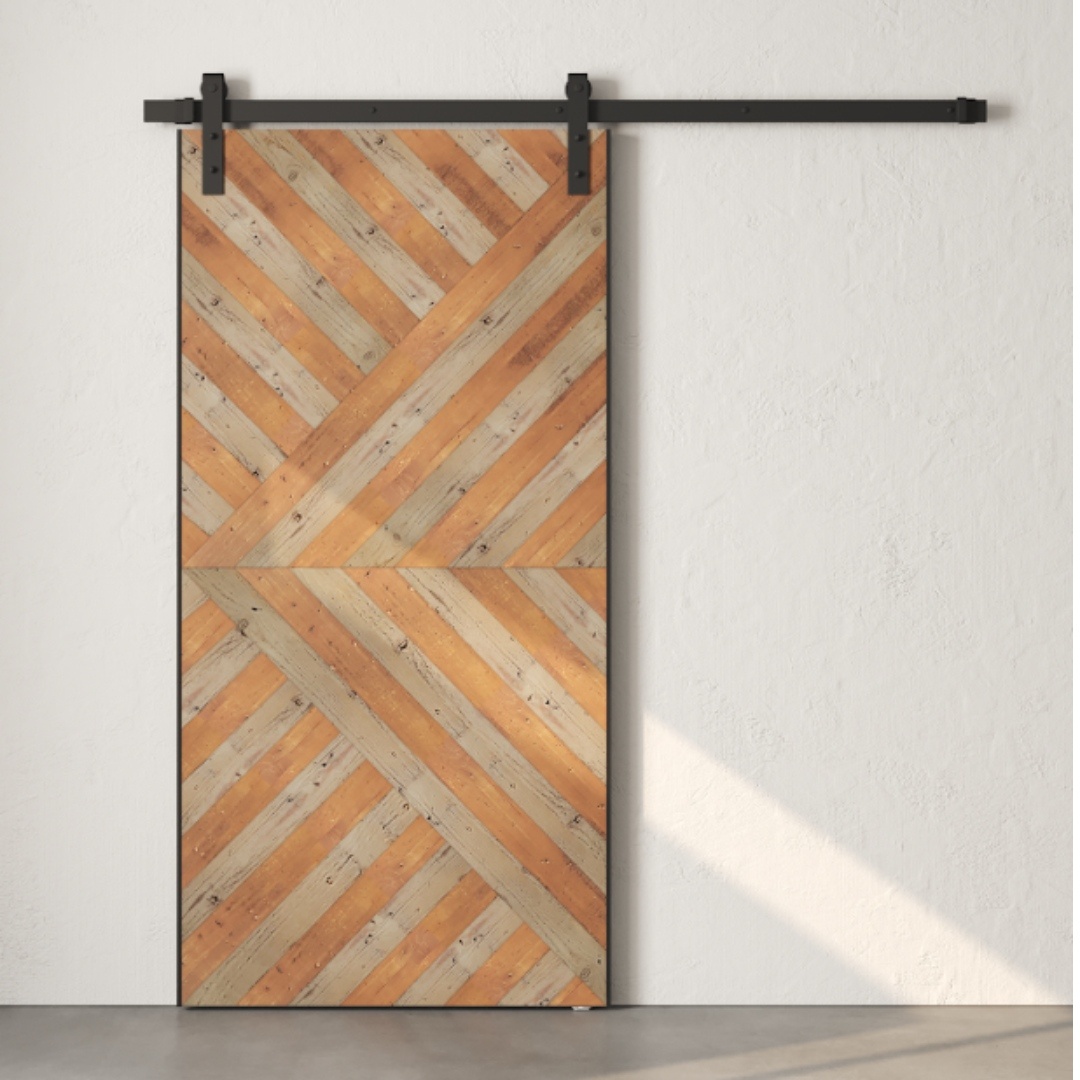 The Celestia Reclaimed Wood Barn Door (Grey), featuring a geometric wooden pattern and black metal hardware, is mounted on a white wall.
