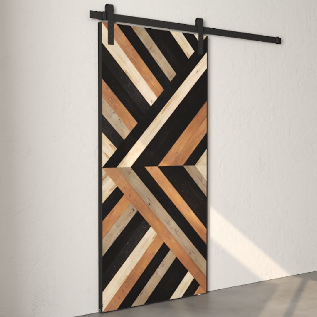 Introducing the Nomad Barn Door, a wooden sliding door featuring a striking geometric design in various shades of wood and black, mounted on a sleek black metal track against a pristine white wall.