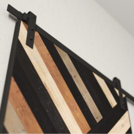 Close-up of the Nomad Barn Door featuring decorative wooden panels with diagonal black, tan, and light brown stripes. The door is attached to the wall with black metal hardware.