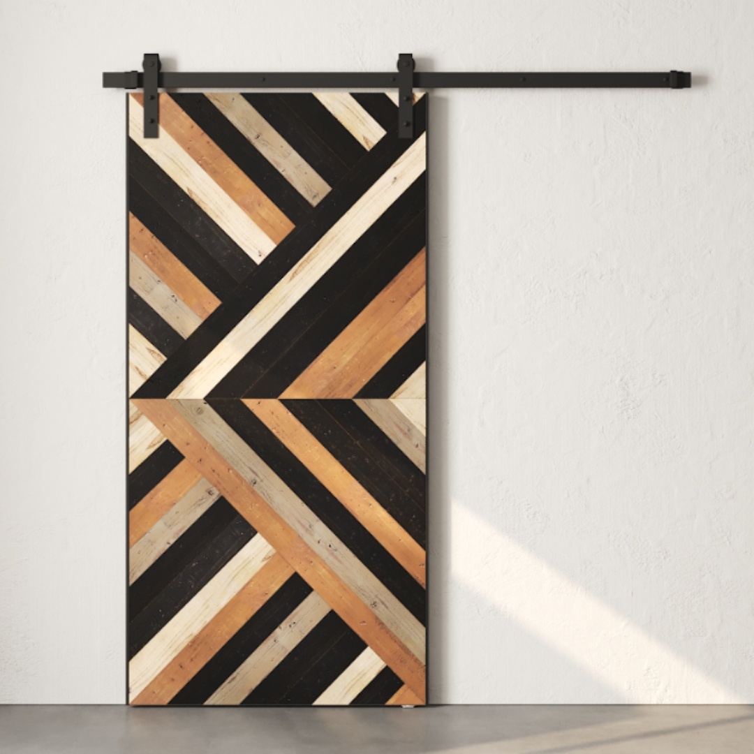 The Nomad Barn Door showcases a striking geometric design featuring diagonal wooden stripes in an array of brown, black, and beige hues, all mounted on a sleek black metal track against a pristine white wall.