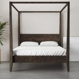 A Riviera Bed (Café Noire) with white bedding is situated in a minimalist room with a light-gray floor, a potted plant, and a framed picture leaning against the wall.