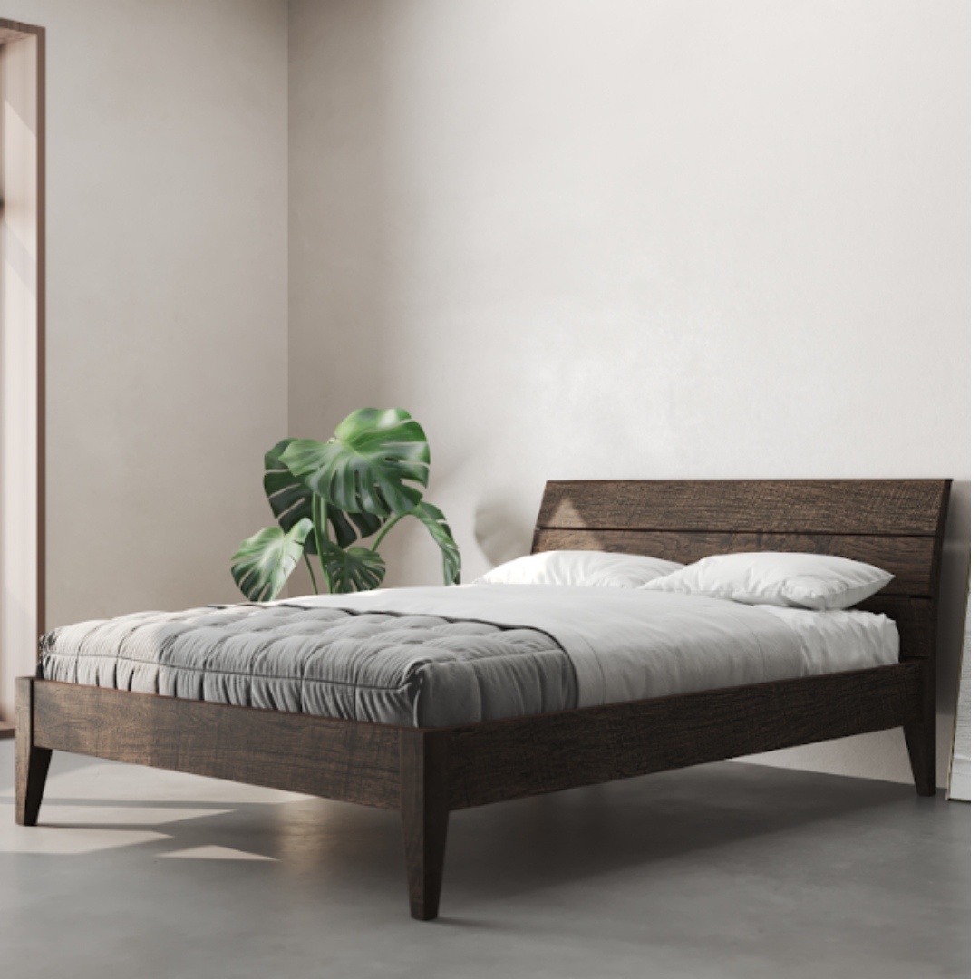 A minimalist bedroom showcases the Tuscan Bed in Café Noire, adorned with white bedding, a grey blanket, two white pillows, and a large green plant in the corner.