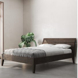 A minimalist bedroom showcases the Tuscan Bed in Café Noire, adorned with white bedding, a grey blanket, two white pillows, and a large green plant in the corner.