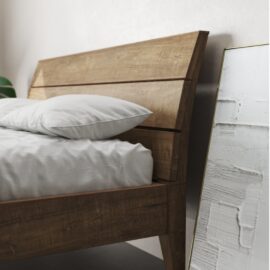 A Tuscan Bed (Natural) adorned with a white mattress and pillows, positioned beside a mirror with a textured white-painted frame, leaning against the wall.