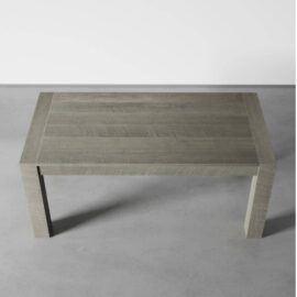 A Villa Dining Table in Rustic Grey is positioned on a grey floor against a white wall.