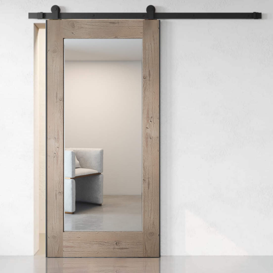 The Beveled Mirror Barn Door in White Wash is partially open, revealing a light-colored chair in the adjacent room.