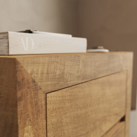 A close-up of the Lugano Nightstand's corner features a light-colored book with a minimalist design and the letters "AD" visible on the spine, along with a small object placed on top.