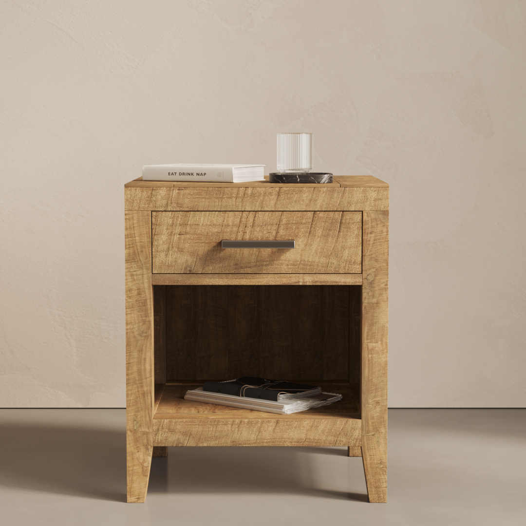 A Riviera Nightstand with one drawer and an open shelf holding magazines, a book, a glass, and a small tray on top, set against a light-colored wall.