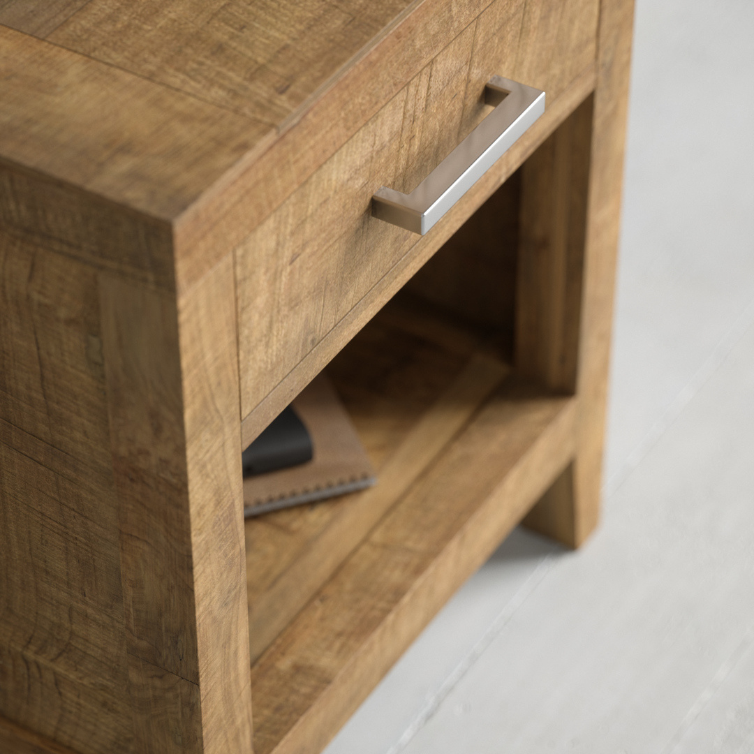 Riviera Nightstand - 2 Close-up of the Riviera Nightstand, featuring a wooden design with a drawer and an open shelf below. The shelf contains a closed notebook and a black object, while the drawer is adorned with a metallic handle.