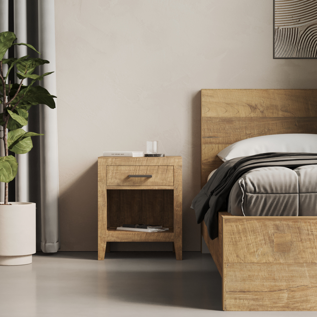 Riviera Nightstand - 3 A Riviera Nightstand beside a matching wooden bed with grey and white bedding. The nightstand features a drawer and an open shelf, with a book and a glass of water on top. A potted plant sits to the left.