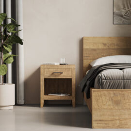A Riviera Nightstand beside a matching wooden bed with grey and white bedding. The nightstand features a drawer and an open shelf, with a book and a glass of water on top. A potted plant sits to the left.