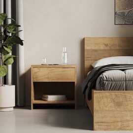A Satillo Nightstand with a glass of water and a few books next to a matching bed in a minimalistic bedroom. A potted plant and part of a painting are also visible.