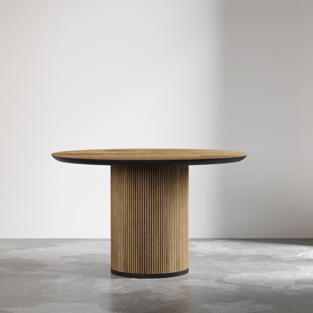 The Bolivar Round Dining Table, featuring a ribbed cylindrical base and a smooth top, stands in an empty room with a light-colored wall and grey flooring.