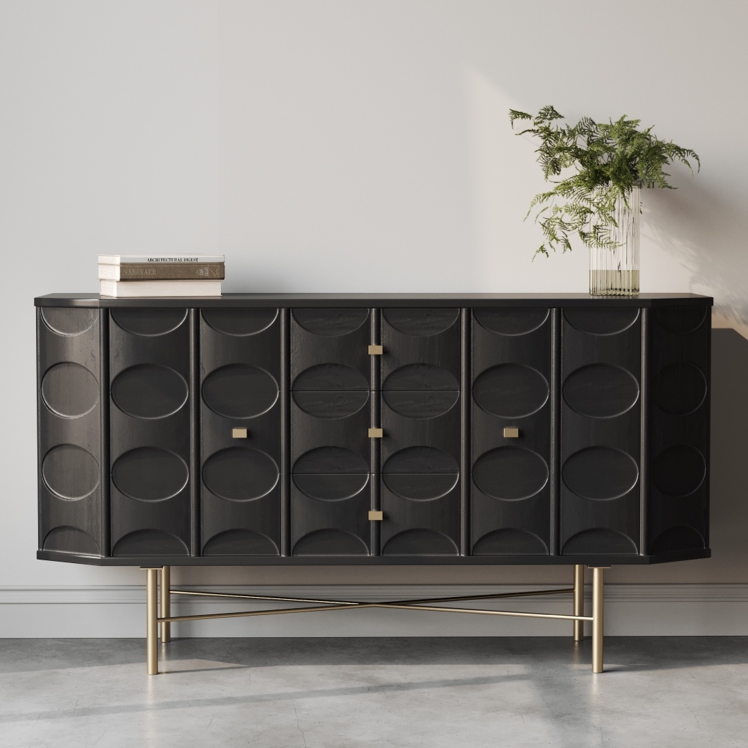 The Alba 60" Side Cabinet, with its sleek black modern design and geometric patterns complemented by gold legs and hardware, sits stylishly against a white wall. A plant in a vase and a stack of books adorn its surface.