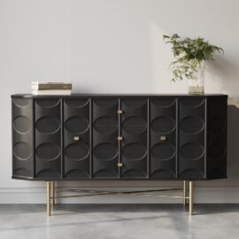 The Alba 60" Side Cabinet, with its sleek black modern design and geometric patterns complemented by gold legs and hardware, sits stylishly against a white wall. A plant in a vase and a stack of books adorn its surface.
