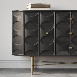 An Alba 60" Side Cabinet with dark, oval-patterned cabinet doors sits against a white wall. A book titled "Architectural Digest" rests on top, while gold legs support the piece over a light-colored floor.