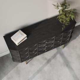 An Alba 60" Side Cabinet, crafted from dark wood and adorned with brass knobs, is placed against a wall. A potted fern and a closed book rest elegantly on top of the sideboard, while the floor is concrete.