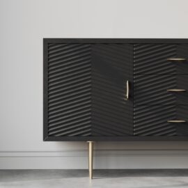 The Arista 60" Side Cabinet in black, boasting gold legs and handles, three drawers, and a ribbed-textured door, stands against a light gray wall on a concrete floor.