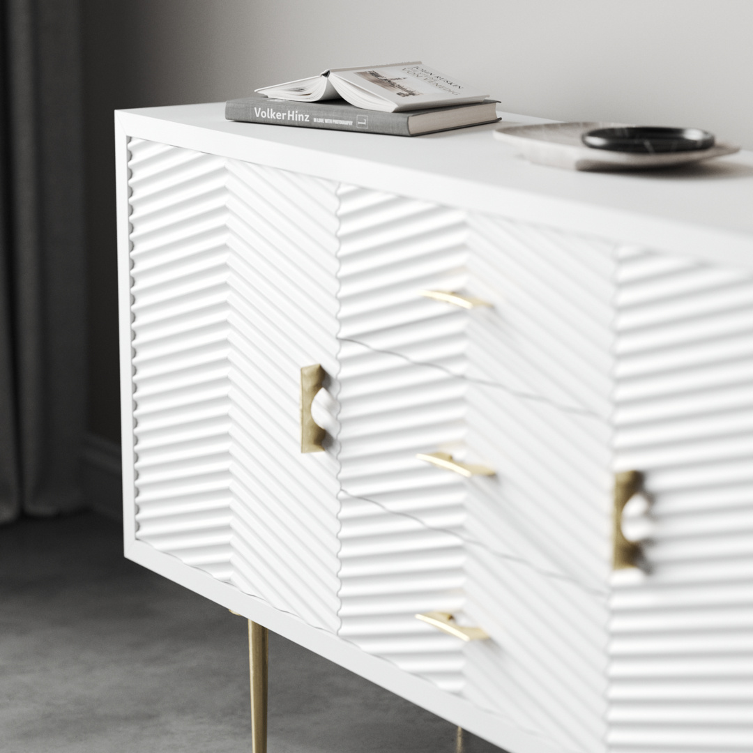 Arista 60_ Side Cabinet 3 The Arista 60" Side Cabinet in White Wash boasts textured doors and sophisticated gold handles, elegantly perched on slender legs. Offering ample space for decor such as books and dishes on its smooth top, it creates a stunning contrast against the gray concrete floor.
