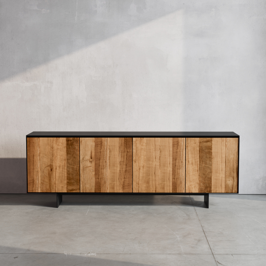 The Atelier Dining Buffet with its minimalist design stands against a plain, light gray wall on a concrete floor. This wooden sideboard features a black top and legs, complemented by front panels made of vertical wooden slats.