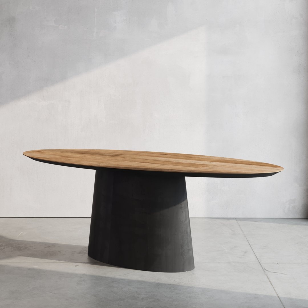 The Atelier Oval Dining Table, featuring a wooden top and a black cylindrical base, is placed in a minimalist room with concrete flooring and a light gray wall.