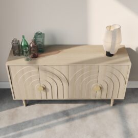 The Azul 58" Side Cabinet, crafted from light wood and featuring two decorated doors, stands against a plain wall on a concrete floor. On top of the cabinet are three azul-colored glass bottles and a modern table lamp.