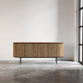 The Bolivar Dining Buffet, a modern wooden sideboard featuring a ribbed design and metal legs, is placed against a plain wall in a room with a large window and concrete floor.