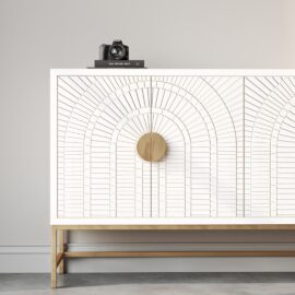A 60-inch white side cabinet named the Coral 60" Side Cabinet, featuring an intricate geometric pattern, gold handles and legs, with a book titled "EAT DRINK NAP," and a camera on top, against a light grey wall. Just imagine how lovely this piece would look with accents of coral in the decor.