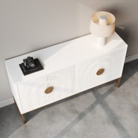 The Coral 60" Side Cabinet in white, featuring two drawers with circular handles and adorned with a lamp and a camera placed on top of a book, stands against a light gray wall. Shadows cast from nearby windows are visible on the floor.