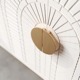 Close-up of a circular, gold-colored door handle on the white, patterned surface of the Coral 60" Side Cabinet featuring a sunburst design.