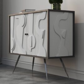 The Estrella 60" Cabinet is a contemporary white unit featuring intricately embossed doors, supported by sleek angled metal legs. Positioned against a simple wall, it is adorned with a green plant for a natural accent.