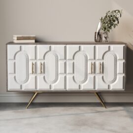The Lugo 60" Side Cabinet, a white rectangular sideboard showcasing ornate geometric patterns, features gold handles and tapered gold legs. Placed against a beige wall, it is stylishly adorned with books and a vase holding greenery.