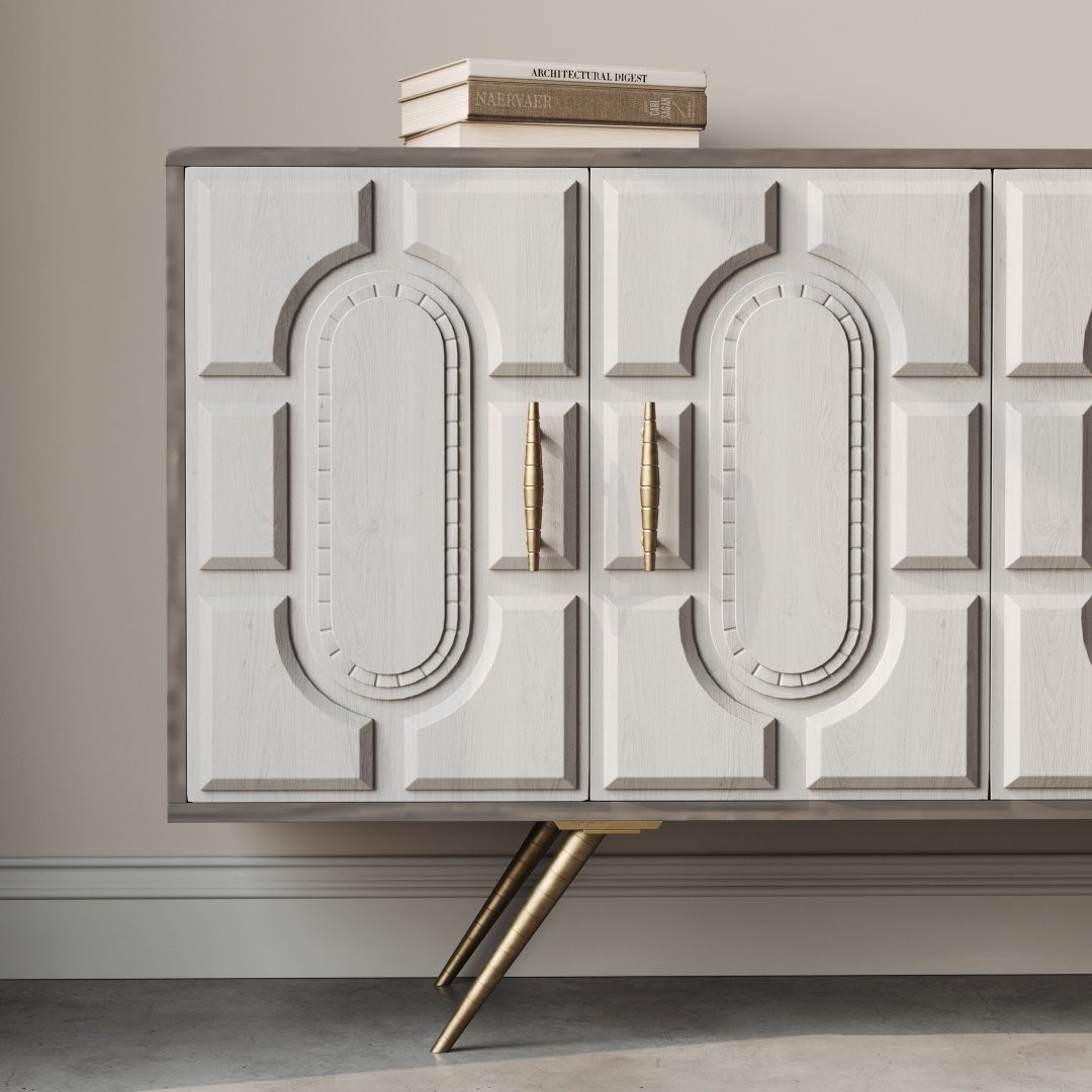 Lugo 60 Side Cabinet-b A close-up view of the Lugo 60" Side Cabinet reveals its light wooden finish, ornate oval patterns, brass handles, and angled brass legs. Two books are placed on top of the cabinet.