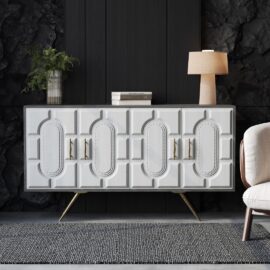 A white Lugo 60" Side Cabinet adorned with geometric patterns, set against a dark wall and topped with a lamp, a small stack of books, and a fern in a vase, next to a beige chair on a gray rug.