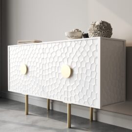 The Luna 60" Side Cabinet features a white sideboard adorned with a striking hexagonal pattern on its doors and accented by large round gold handles. It stands gracefully on slender gold legs and is topped with decorative items such as a coral display and a bowl.