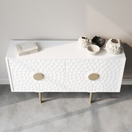 A Luna 60" side cabinet in white textured finish, equipped with circular handles, stands against a light gray wall on a concrete floor. Its surface showcases three decorative vases and two books, adding an elegant touch to any space.