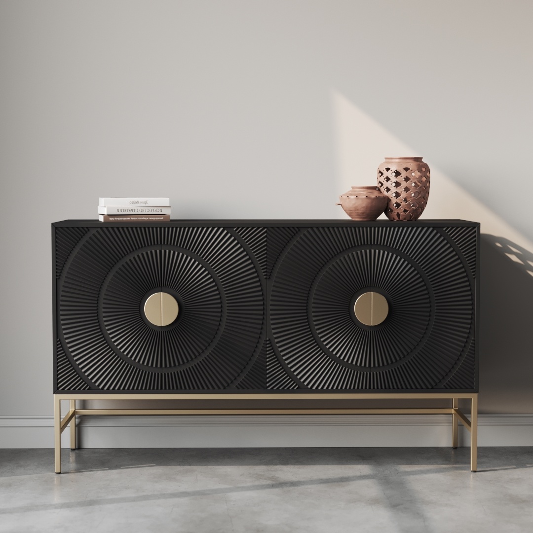 A black, modern sideboard with textured circular patterns and gold handles stands against a light gray wall on a concrete floor. This piece, known as the Orbita 60" Side Cabinet, holds two pink vases and a stack of white books, perfectly blending style and function into its frame.
