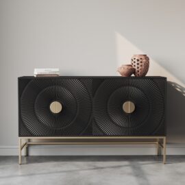A black, modern sideboard with textured circular patterns and gold handles stands against a light gray wall on a concrete floor. This piece, known as the Orbita 60" Side Cabinet, holds two pink vases and a stack of white books, perfectly blending style and function into its frame.