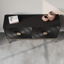 A black Orbita 60" Side Cabinet, featuring circular patterns on its doors, stands on gold legs. A book and two decorative vases rest on top of it. The setting is minimal and modern, with a concrete floor.