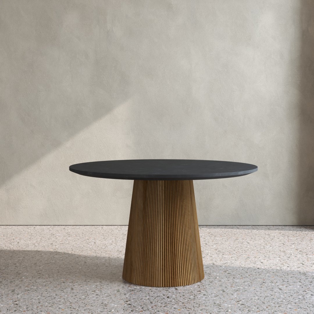 The Osaka Round Dining Table, featuring a black top and a brown, ribbed conical base, stands in front of a light gray wall on a speckled floor.
