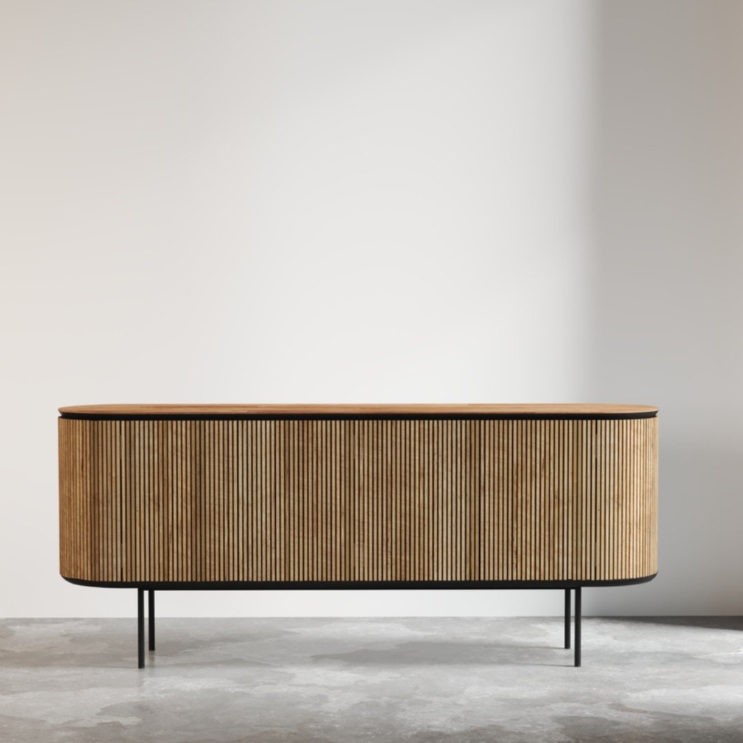 Untitled-design-1.jpg The Bolivar Dining Buffet, featuring a modern design with vertical wooden slats, a sleek black frame, and slender legs, stands against a plain light-colored wall in a minimalist room.