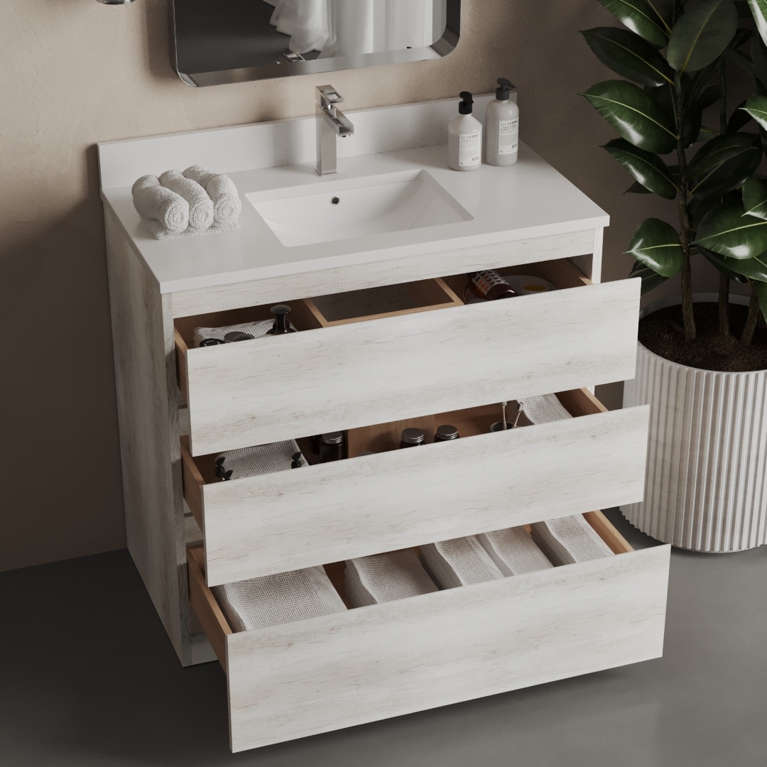 A rustic white vanity with a single sink, a mirror above, and three open drawers filled with towels and toiletries. A large potted plant stands next to it, enhancing the serene bathroom ambiance.