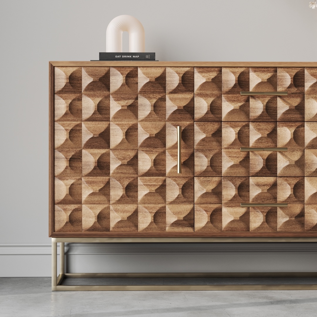 Wadi 57 Side Cabinet-b The Wadi 57" Side Cabinet, a wooden piece with geometric patterned doors and drawers highlighted by brass handles, stands against a light gray wall. A sculpture and a book are placed on top.