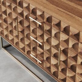 Close-up of the Wadi 57" Side Cabinet, crafted from wood and showcasing a striking geometric carved design. It features three central drawers and two side doors, each adorned with sleek metal handles.