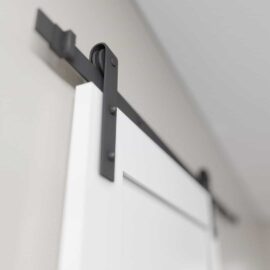 A close-up view of a 3-Panel Barn Door in white, suspended from a black metal track system against a light-colored wall.