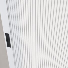 Close-up of the Celine Oval Flutted Panel Barn Door, featuring a white, vertically ribbed design and a black recessed handle on the left side.